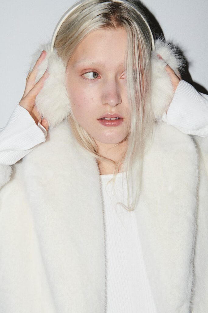 Model wearing white faux fur earmuffs and jacket.