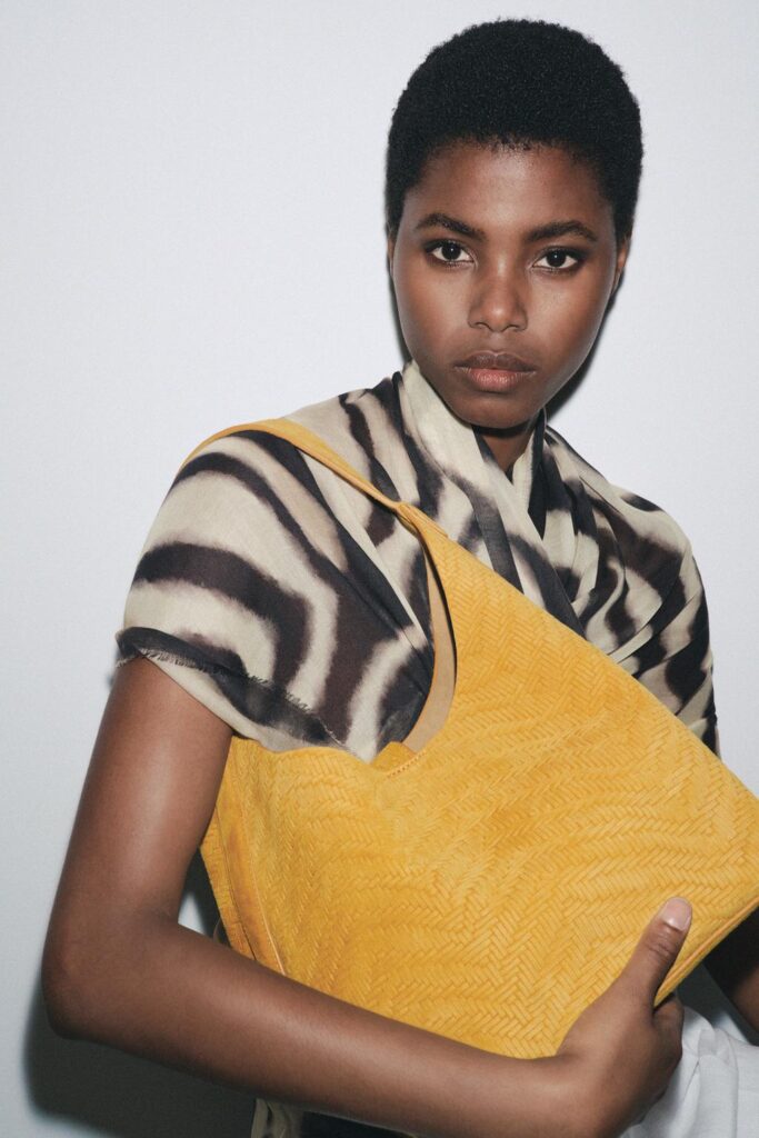 Woman wearing patterned shawl and holding yellow shoulder bag.