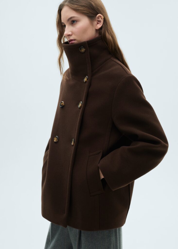 Side view of a model in a brown funnel-neck jacket.