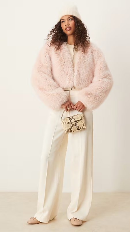 Model wearing light pink faux fur jacket, white pants and printed small bag.