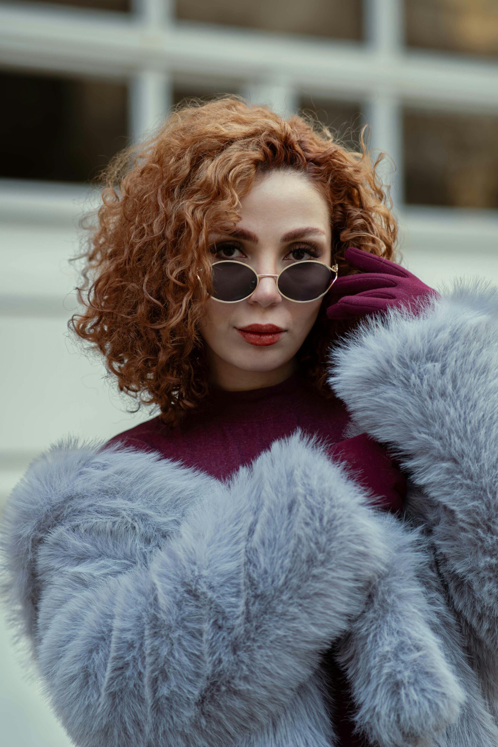 Woman in a faux fur jacket peeking over sunglasses.