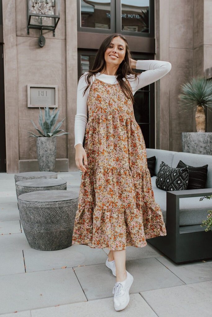 Woman wearing a sundress layered with a sweater underneath.