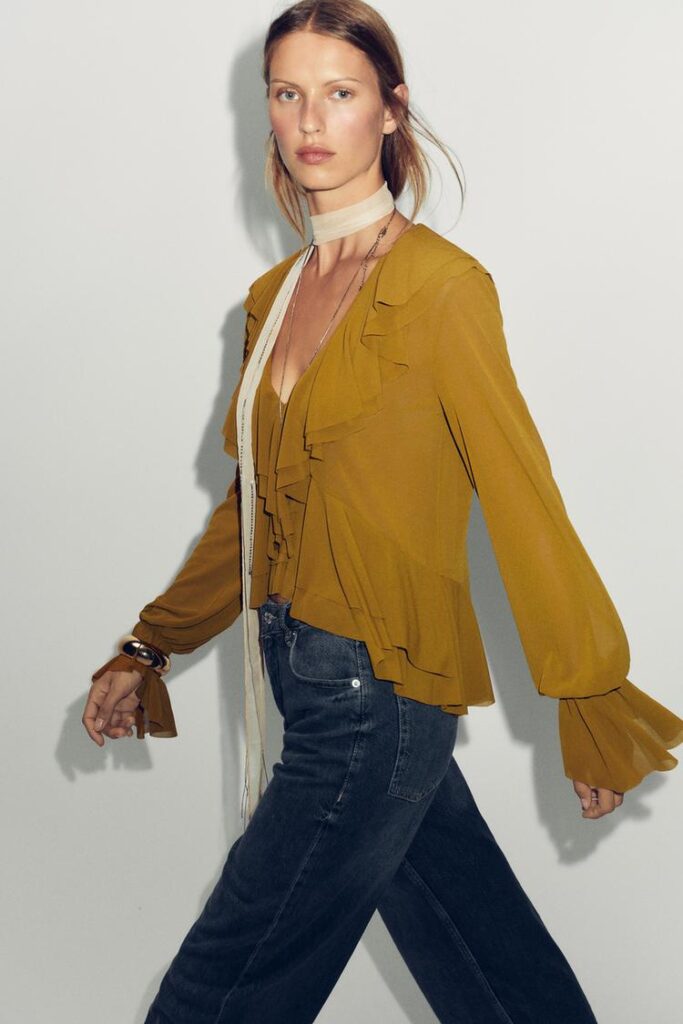 Model wearing a yellow ruffle blouse paired with jeans and a thin scarf. 