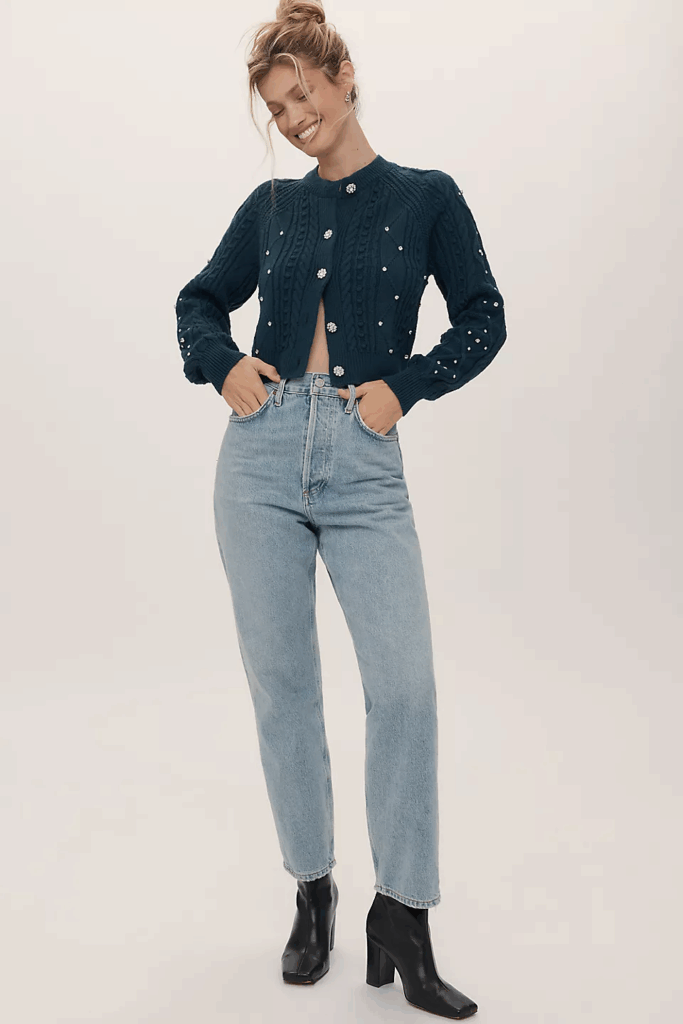 Smiling model wearing a blue knit cardigan, jeans, and ankle boots. 