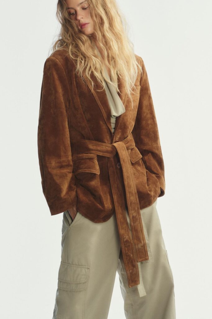 A model styled in a brown suede leather jacket as the highlight of her outfit.
