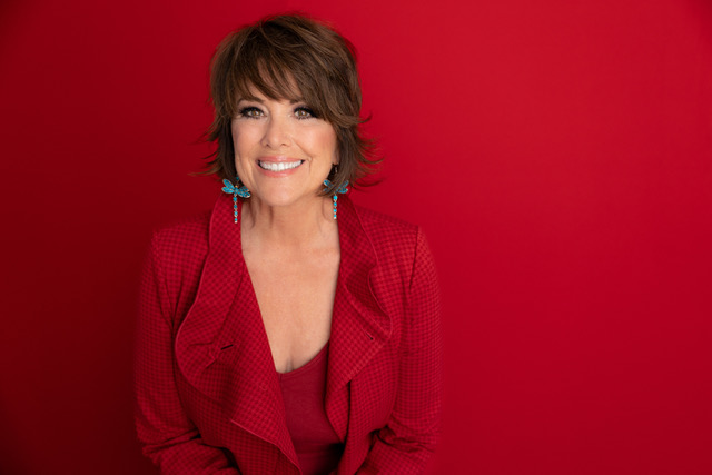 A woman wearing professional red attire against a red wall background.