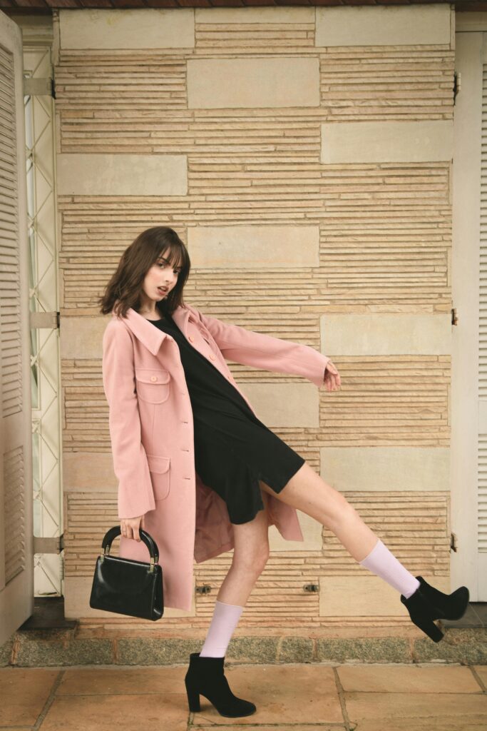 Model wearing a soft, polished outfit with all-black clothing and accessories topped with a long pink jacket.