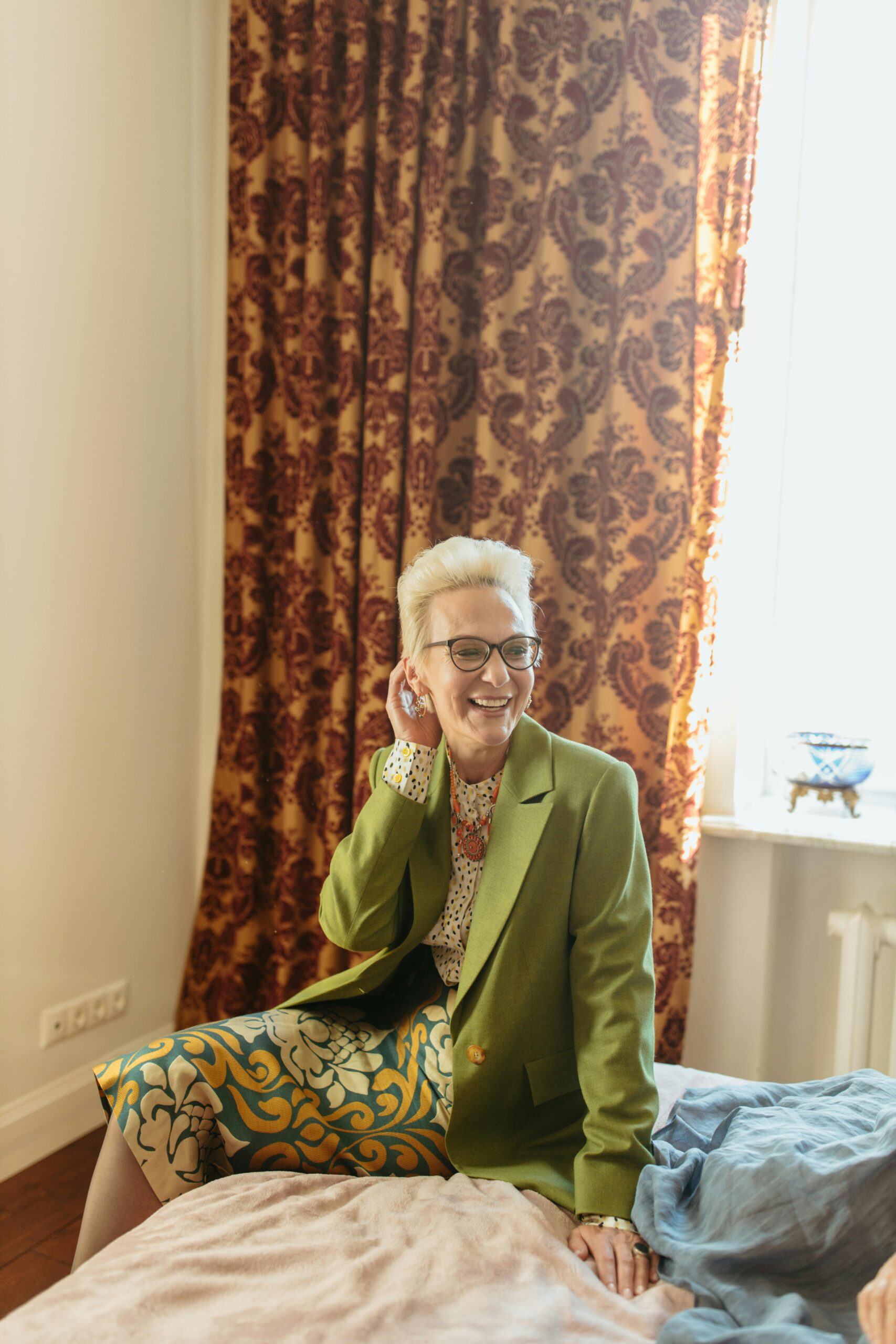Smiling woman sitting on a bed wearing a patterned outfit recommended by a personal stylist in Albuquerque.