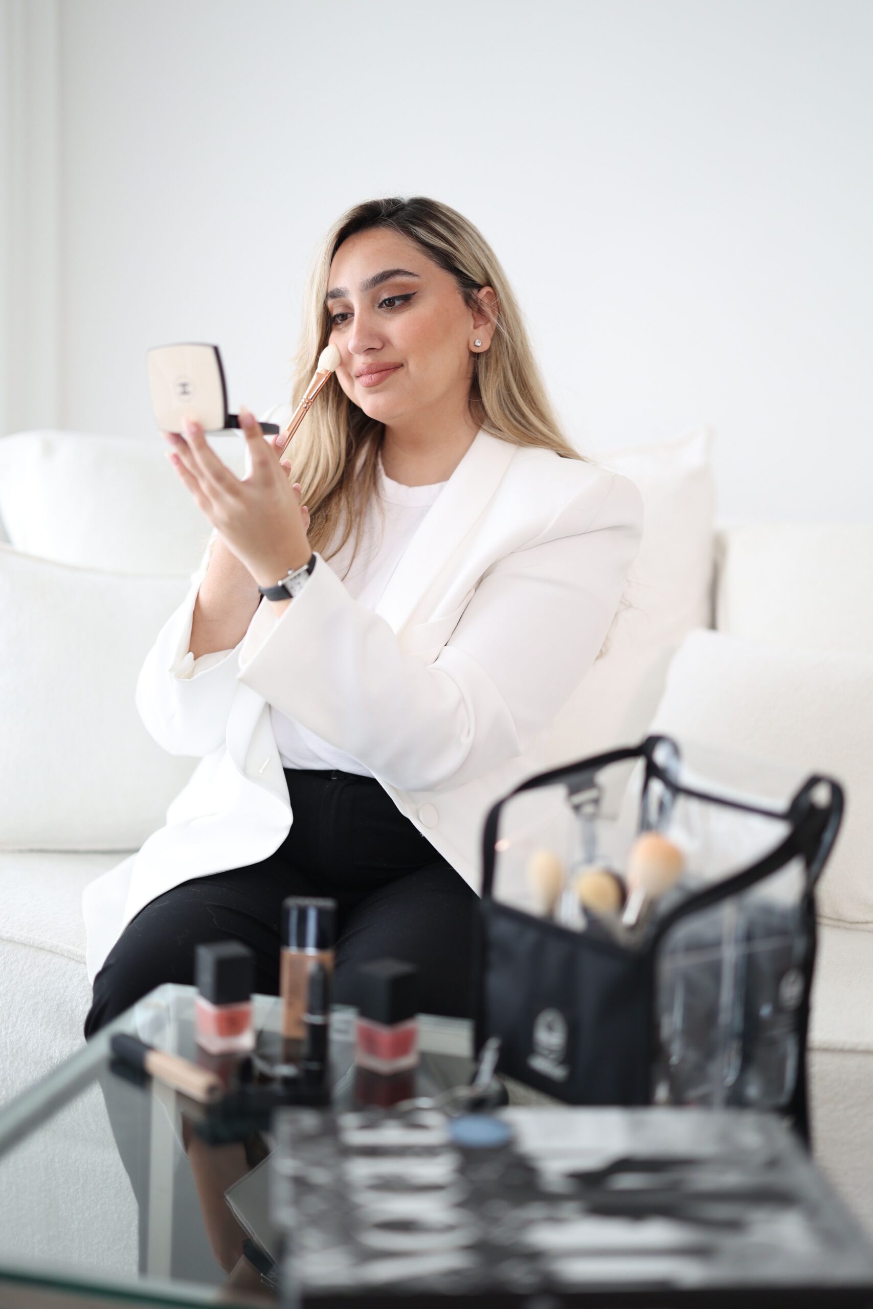 A woman applying makeup while sitting on the couch.