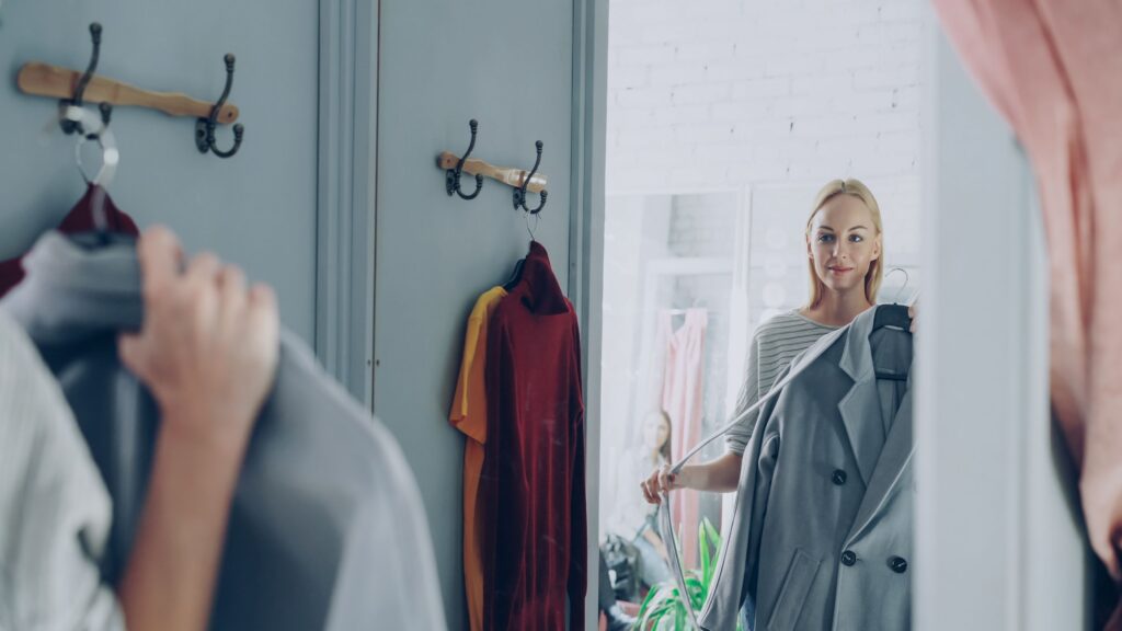 Woman trying on a coat in front of a mirror.